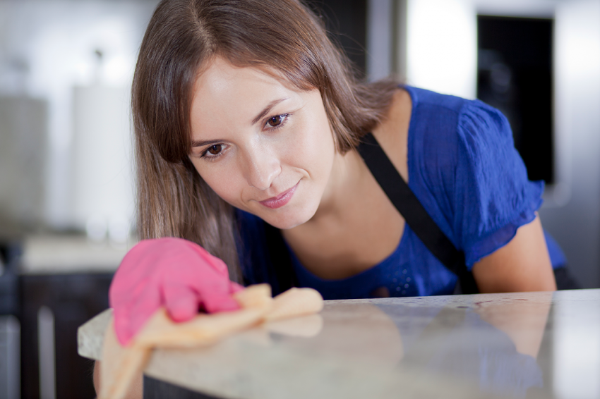 Pure clean. Young positive afro american house maid in apron cleaning table  in the modern kitchen. Professional female cleaner at work Stock Photo