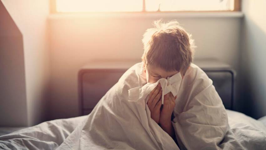 How to Clean Your Home After Being Sick Person sneezing into a tissue to limit germ spread at home